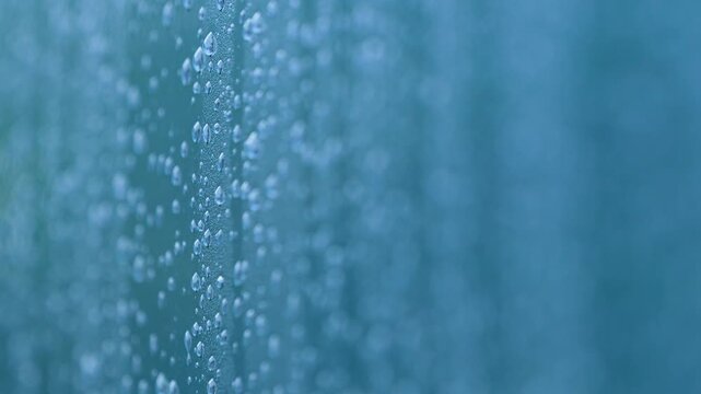 A detailed macro perspective of water droplets clinging to a blue window pane. This minimalist, authentic footage captures the essence of wellness and calm reflection after rainfall.