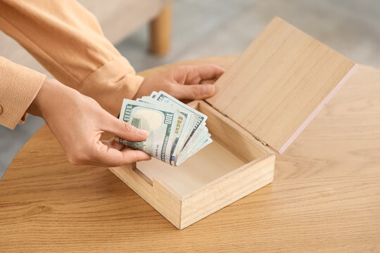 Personal savings and financial planning, person putting cash into a wooden box for emergency fund or budget management on a table