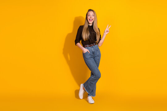 Young woman in casual outfit poses with peace sign against bright yellow background