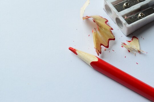 Colored pencil and sharpener. Close-up of a sharpened red pencil on a white background