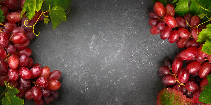 Gorgeous red grapes with green beautiful leaves on a gray board as an elegant background for everything to do with wine