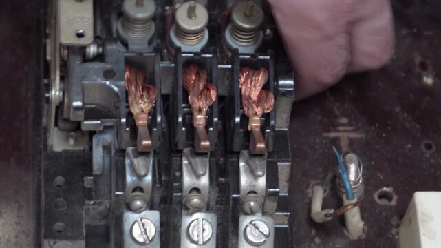 Close up of hands repairing retro three-phase electrical contactor mechanism, A man inspects the internal components of an old high-voltage magnetic switch from a control panel.