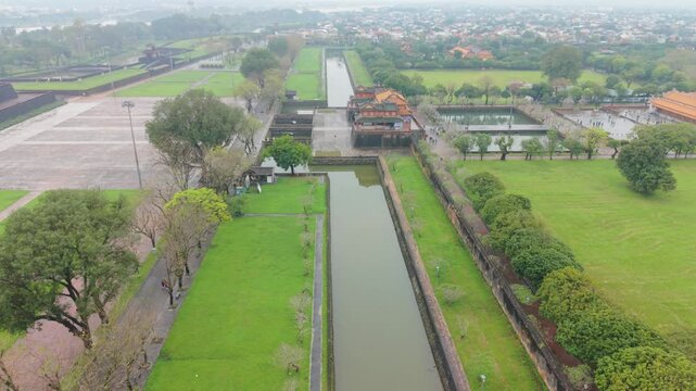 Visitors Walk Through Open Plaza. Adjacent Ponds Border Stone Path. Steps And Ponds Guide Travelers Toward Gateway. People Cross Stone Causeway With Bridges And Visit Surrounding Ponds