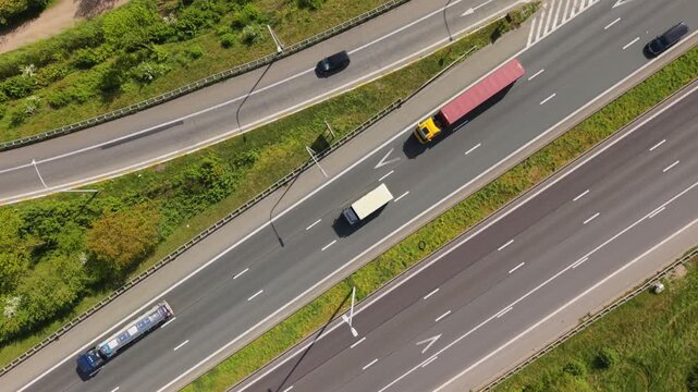 Aerial perspective captures various vehicles such as trucks and cars navigating a busy highway, with lush greenery lining the road, illustrating the dynamic flow of traffic and infrastructure