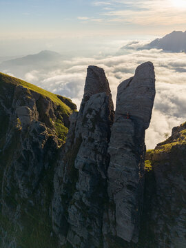 Aerial view of Punta Carina, a dramatic rock formation rising above a sea of clouds in the Apuan Alps with rugged stone textures and golden sunlight in Minucciano, Toscana, Italy.