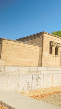 A vertical pan shot of the Temple of Debod, an ancient Egyptian temple relocated to Madrid, Spain. Featuring stone architecture and lush green trees under a bright sun.