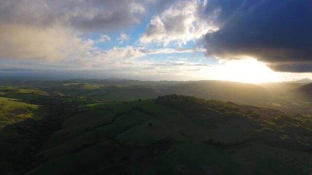 Aerial view of rolling hills of Tuscany bathed in the warm light of the golden hour with dramatic clouds, Tuscany, Italy.