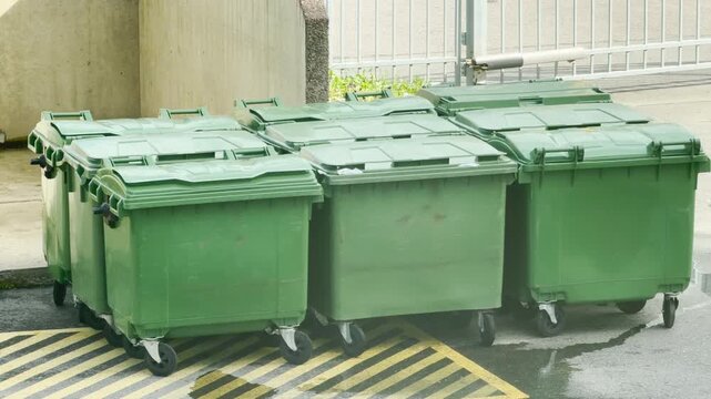 Green trash bins stand neatly in a row near a concrete wall. Their orderly arrangement brings a sense of clean responsibility to the quiet outdoor space.