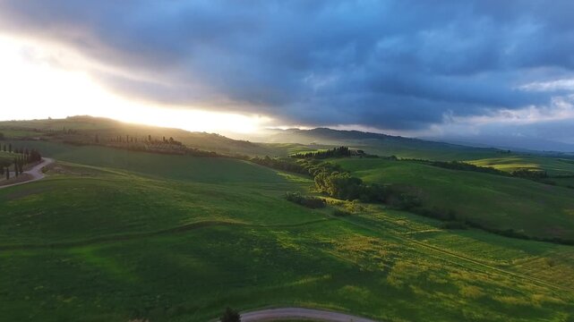 Aerial view of rolling green hills in Tuscany at sunset with dramatic clouds and golden light in Tuscany, Italy.