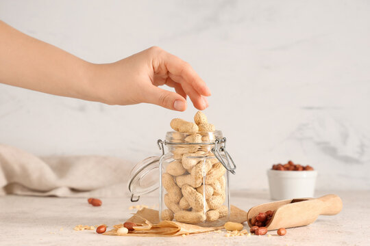 Female hand with glass jar and scoop of peanuts on light table