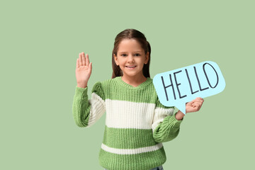 Cute little happy girl holding paper speech bubble with word HELLO while waving hand on green background © Pixel-Shot