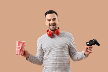 Handsome man with game pad and popcorn on beige background © Pixel-Shot