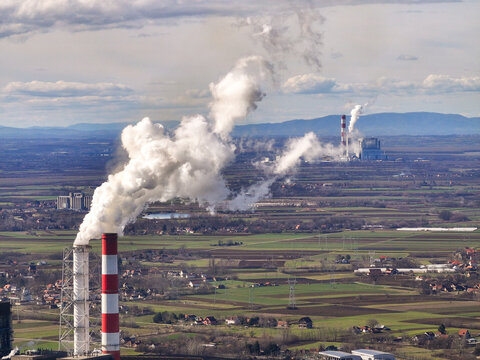 Aerial view of Nikola Tesla Power Plant A with tall chimneys emitting smoke over the surrounding agricultural fields and rural landscape in Urovci, Grad Beograd, Serbia.