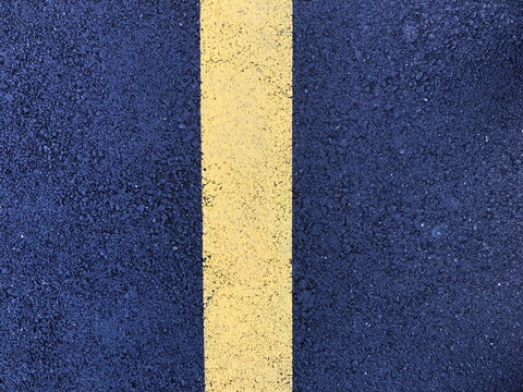 asphalt pavement with vertical yellow road markings in the center. The asphalt texture is grainy, with small inclusions