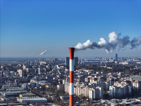 Aerial view of a prominent red and white industrial chimney emitting smoke over the dense urban skyline of Belgrade, City of Belgrade, Serbia.