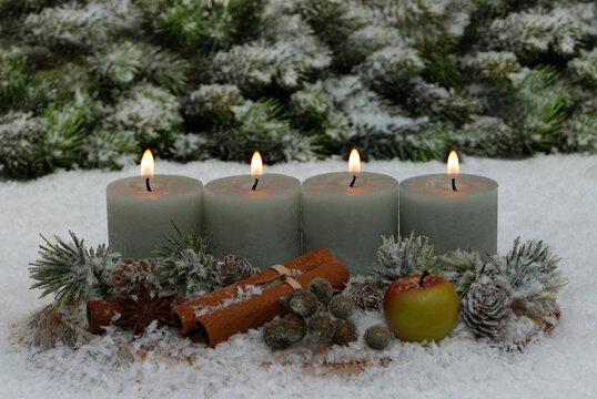 A natural Advent arrangement on a wooden disc in the snow. Four candles are lit for the 4th Sunday of Advent.