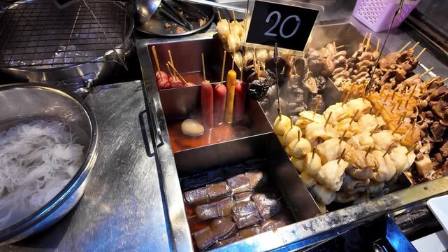 Close up of various meat, fish balls and sausages on skewers cooking in hot spicy broth at a traditional market in Thailand.