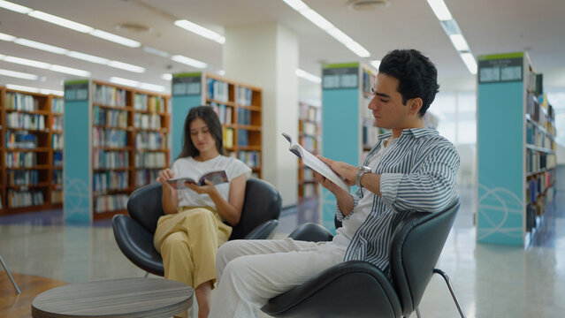 Two students sit comfortably in modern black egg chairs, engrossed in reading books in library