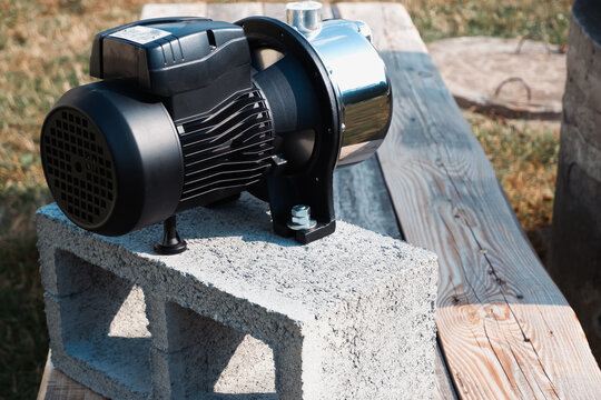 Stainless steel surface water pump mounted on concrete cinder block placed on wooden table outdoors