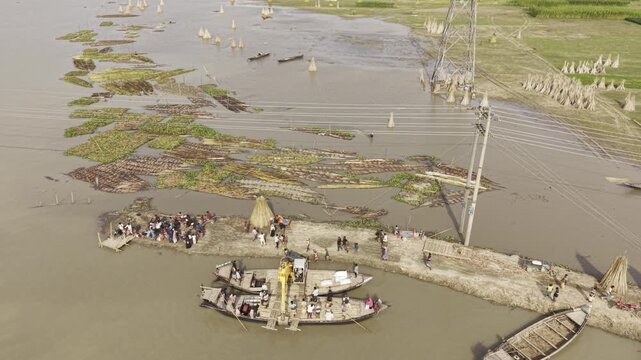 Aerial footage captures an excavator barge crossing the Padma River, with passenger boats and people nearby, floating vegetation, power lines, green fields and a rural village landscape