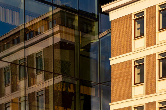 Historic brick building appears through reflections on a modern glass facade creating a layered contrast between old and contemporary urban architecture