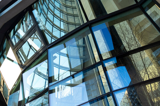 Geometric glass structure and reflective windows create layered architectural lines and blue urban reflections beneath a modern transparent canopy