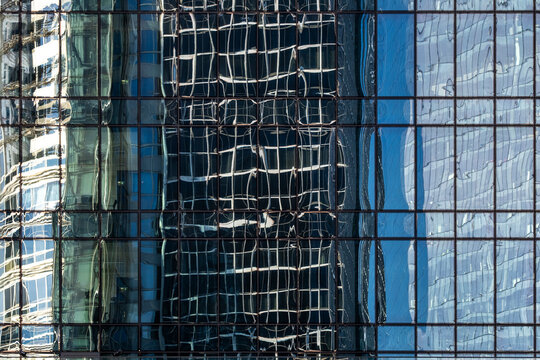 Distorted reflections ripple across blue glass facades creating an abstract architectural pattern of modern buildings and layered urban geometry