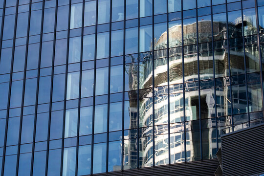 Reflective office windows mirror a curved modern building across a blue glass facade creating an abstract urban architecture pattern in daylight