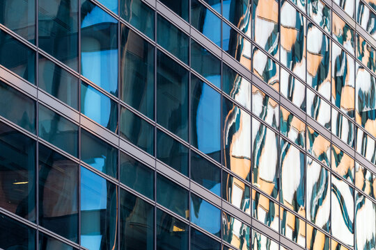 Reflective glass facades create layered architectural patterns with distorted building reflections across a modern urban office exterior in daylight