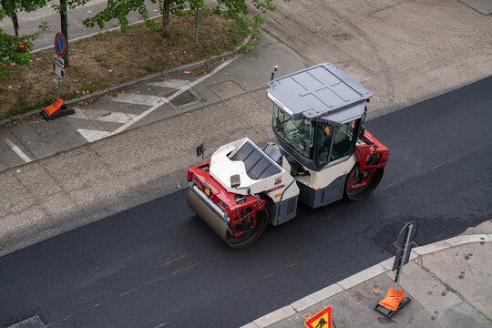 Heavy road roller compactor flattening fresh asphalt layer on urban street, industrial construction machinery resurfacing road, maintenance work site top high angle view, Turin, Italy, August 28, 2026