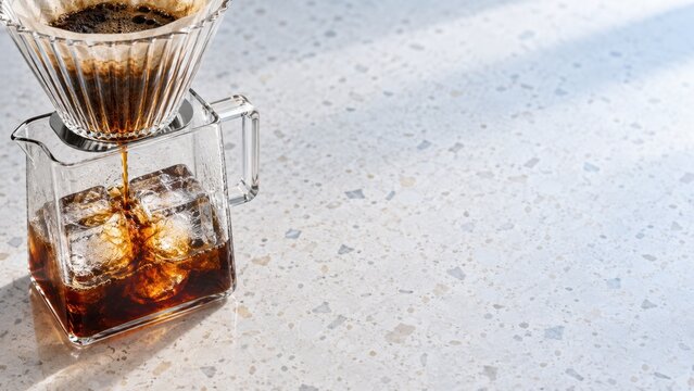 Brewing fresh cold drip coffee with glass coffee maker and ice cubes on terrazzo countertop surface
