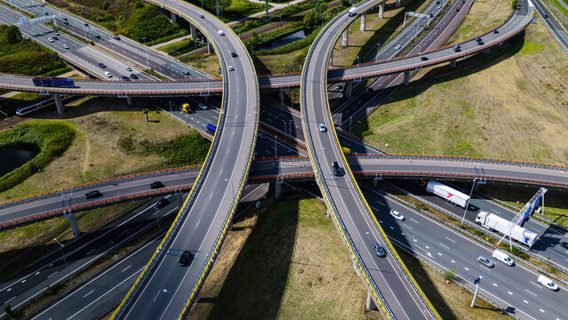 Aerial view of the Westvliet highway intersection featuring multi-level roads with flowing traffic, trucks, and cars, surrounded by green fields in Den Haag, Zuid-Holland, Netherlands.