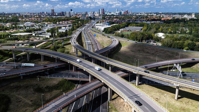 Aerial view of the Westvliet highway intersection with concrete overpasses, flowing traffic, and green landscapes leading to the city skyline in Den Haag, Zuid-Holland, Netherlands.