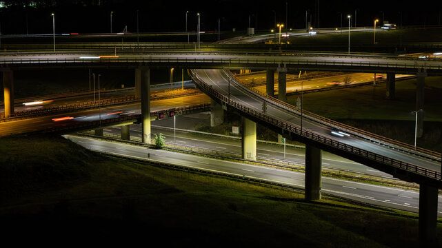 Aerial view of Westvliet highway intersection at night with illuminated roads, light trails from moving vehicles, and concrete overpasses in Den Haag, Zuid-Holland, Netherlands.
