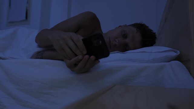 Man trying to sleep but reaching for smartphone to scroll at night, compulsive phone checking, digital addiction and insomnia