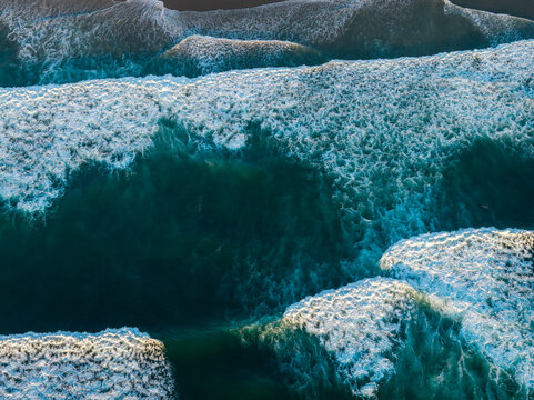 Aerial view of crashing waves of the Pacific Ocean with white foam patterns and deep blue water in Bandon, Oregon, United States.