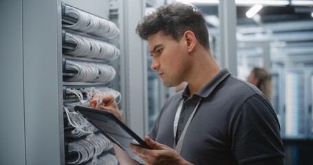 Fototapeta premium Male Network Technician Audits Patch Panel Connections While Referencing Tablet, Checking Cable Identification and Physical Ports During Digital Verification of Data Center Infrastructure Work.