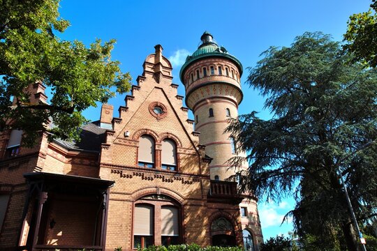 Wiesbaden, Hesse, Germany &ndash; Historic Biebrich Water Tower with ornate brick facade and distinctive round tower framed by green trees.
