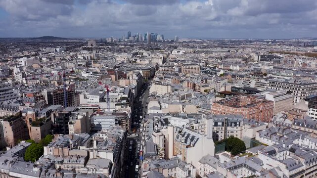 Aerial view of the historic city skyline with dense urban architecture and rooftops under a cloudy sky in Paris, Ile-de-France, France.