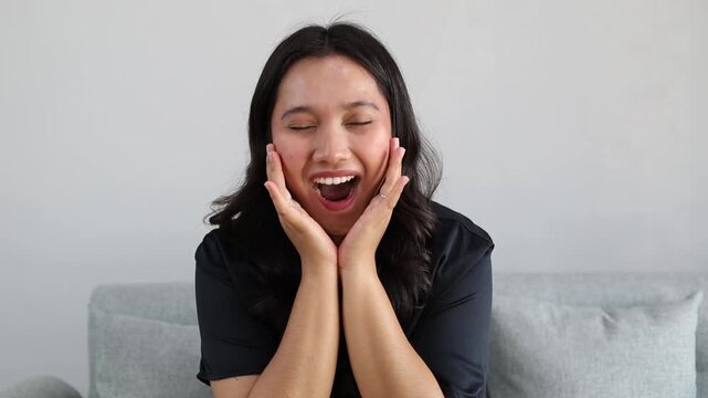 Young attractive Asian woman at home raising eyebrows and opening mouth with surprise after seeing something unexpected