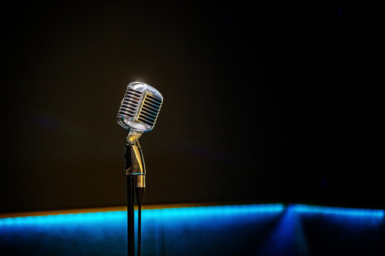 Retro microphone on stage against dark background with blue neon light. Concert, karaoke, stand-up comedy show and public speech concept. Music entertainment venue.
