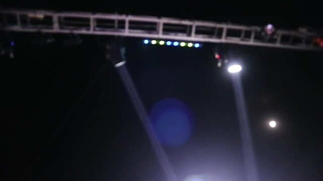Bright stage lights shining down from a metal truss structure in the dark.