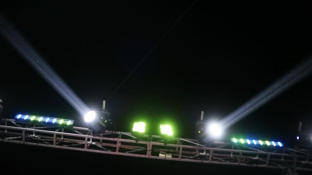 Bright stage lighting equipment shining beams of light into the dark night sky.