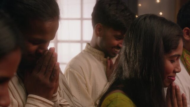 South Asian young adults praying together with folded hands during traditional festival celebration at home. Perfect for cultural holiday campaigns and diverse family storytelling videos