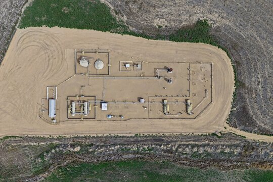 Aerial view of an oil and gas production facility with storage tanks and pipelines on a dirt pad surrounded by agricultural fields in Longmont, Colorado, United States.