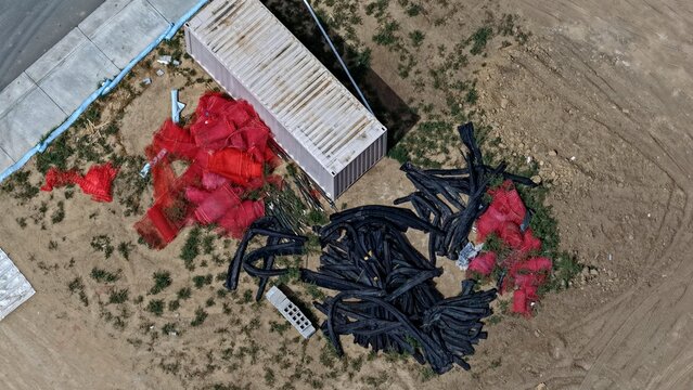 Aerial view of a construction site featuring a white shipping container, piles of red construction netting, and black drainage pipes on a dirt lot in Longmont, Colorado, United States.