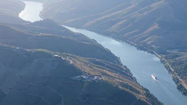 Drone view of a tourist boat on the Douro River in Douro Valley, Portugal, with vineyards and morning reflections. Rising pedestal up drone shot