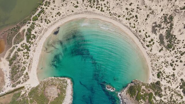 Drone shot of the striking semicircular Voidokilia Beach, turquoise waters, golden sand, and surrounding Mediterranean landscape under bright daylight.