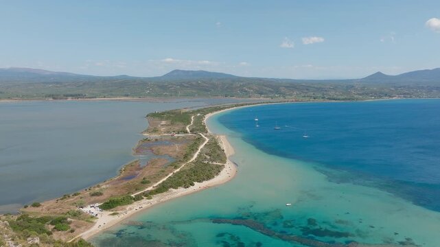 Drone shot over Sykia and Chrisi Ammos beaches near Voidokilia, Pilos. Turquoise waters, sandy isthmus, dramatic coastline, and lush hills under bright daylight sky.