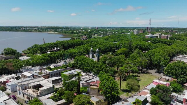 Aerial footage capturing the Basilica of the Holy Sacrament surrounded by dense green foliage, urban rooftops, and river coastline under vibrant daylight and clear skies.